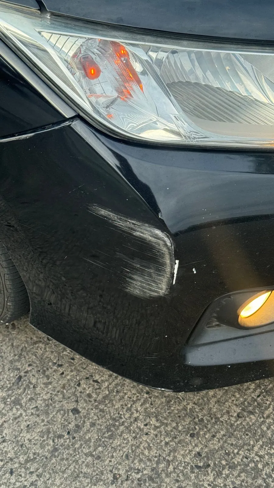 Black car front bumper corner and headlight with a deep scrape and a crack
