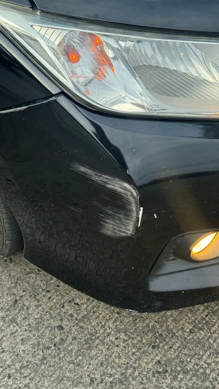 Black car front bumper corner and headlight with a deep scrape and a crack