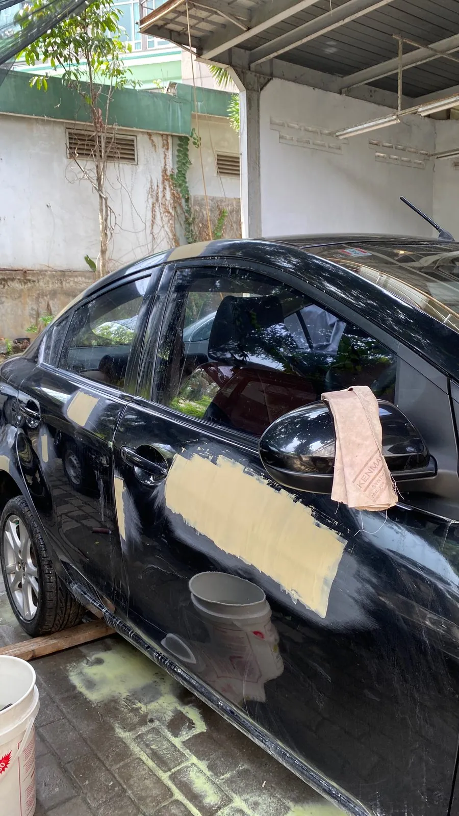 Black Mazda sedan with the driver door skimmed in filler and masking tape