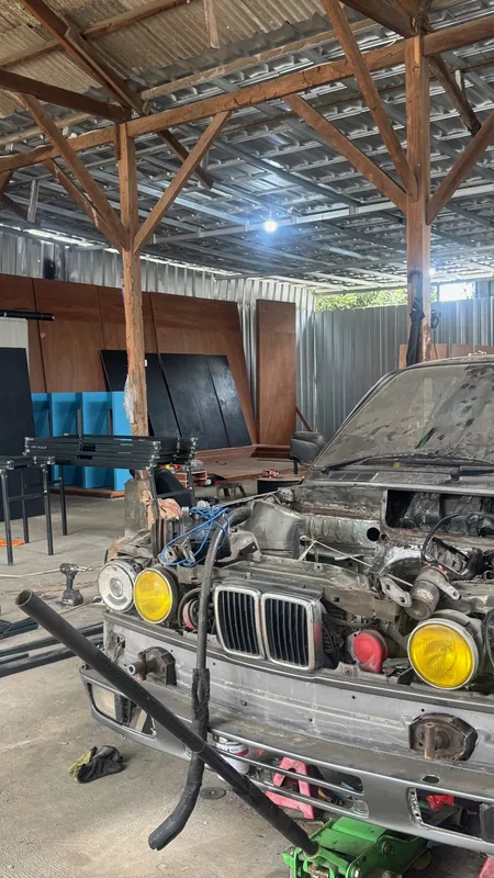 E30 front end with the engine out and yellow headlamps, in the workshop shed