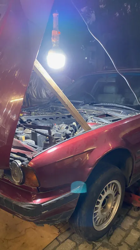 Maroon BMW E34 with the bonnet propped and a work lamp over the engine bay