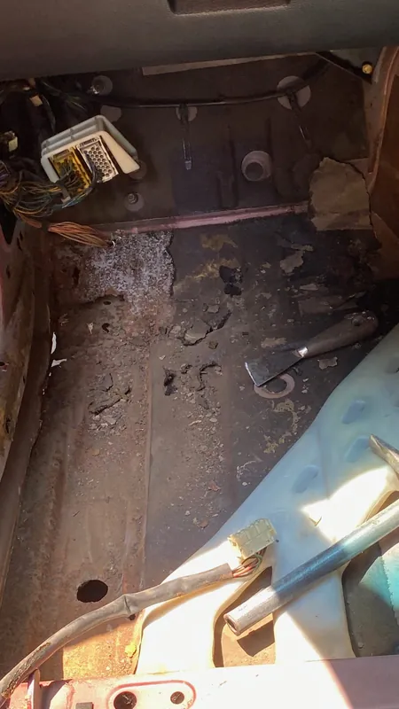 Rusty bare floor pan of the maroon E34 with a hole, interior stripped