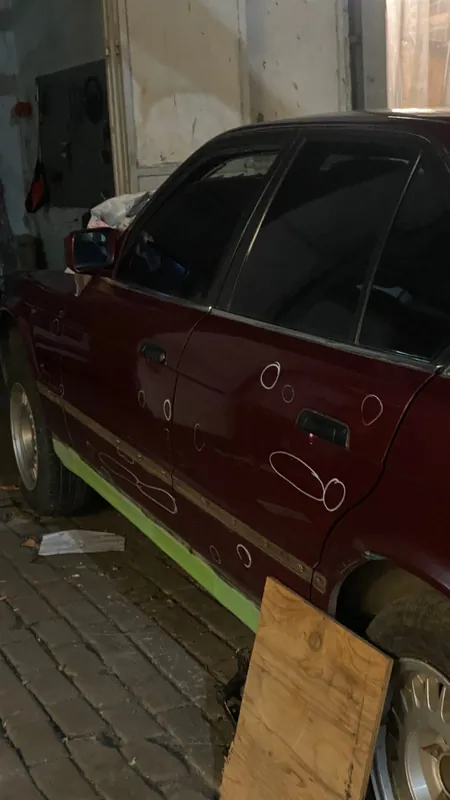Side of the maroon E34 with tape under the sill and a wooden board