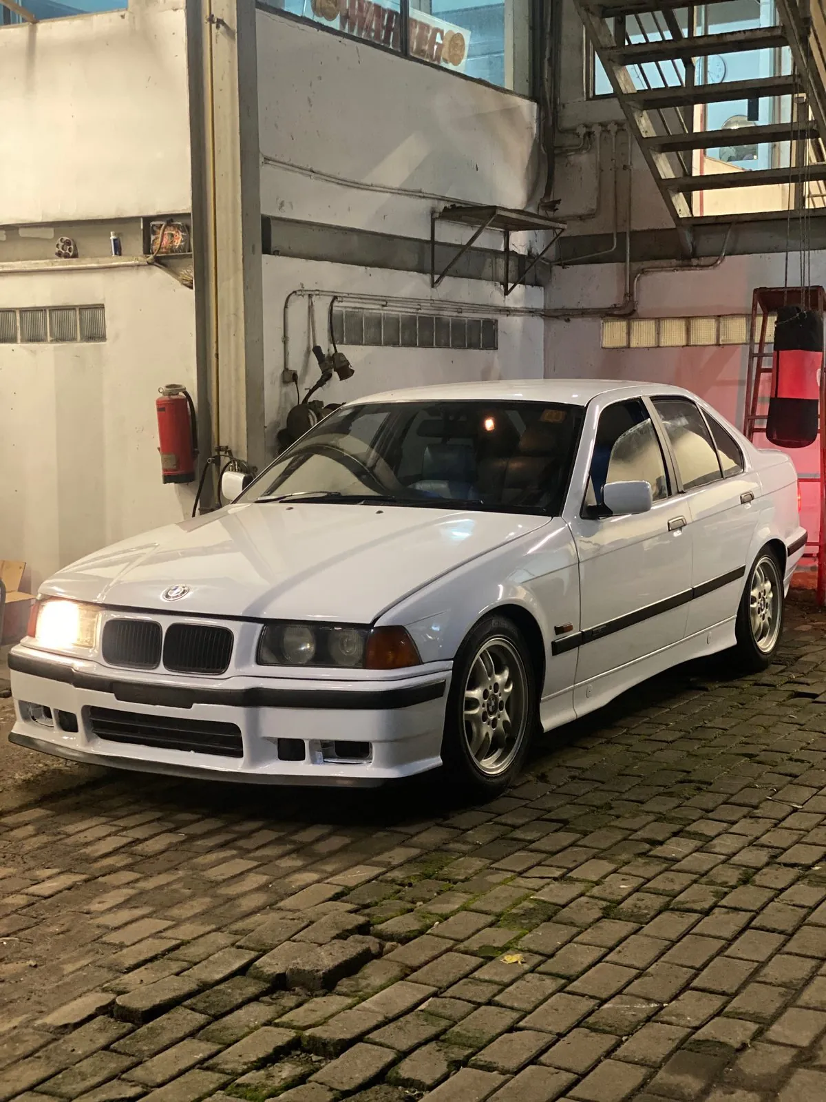 Finished white E36 sedan front three-quarter in the workshop with multi-spoke style alloy