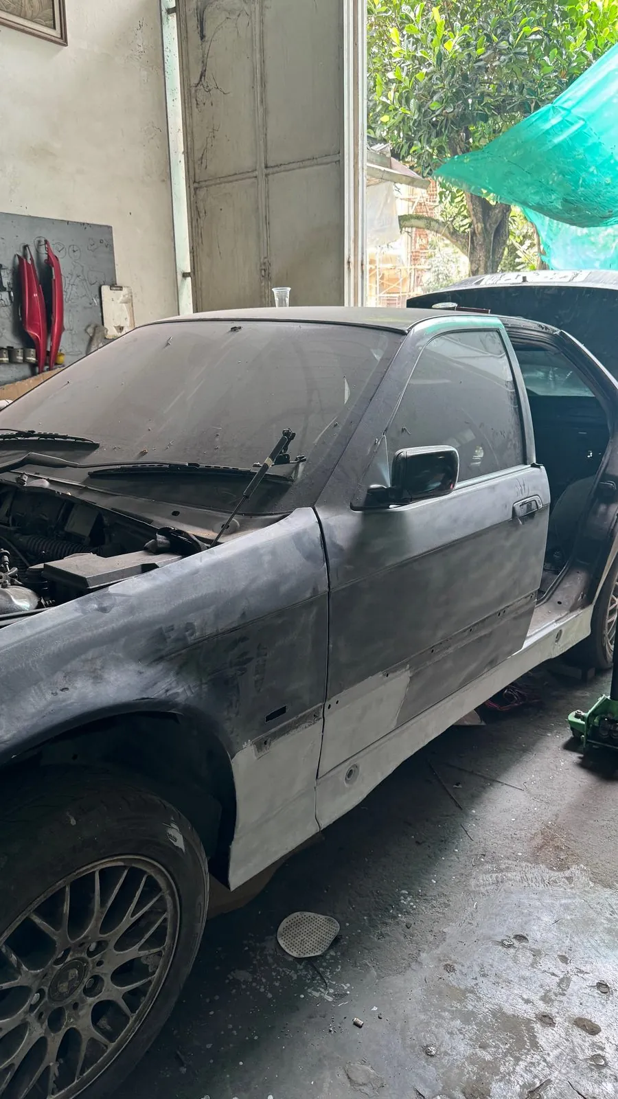 BMW E36-type sedan in the workshop bay with the front wing and door in grey primer