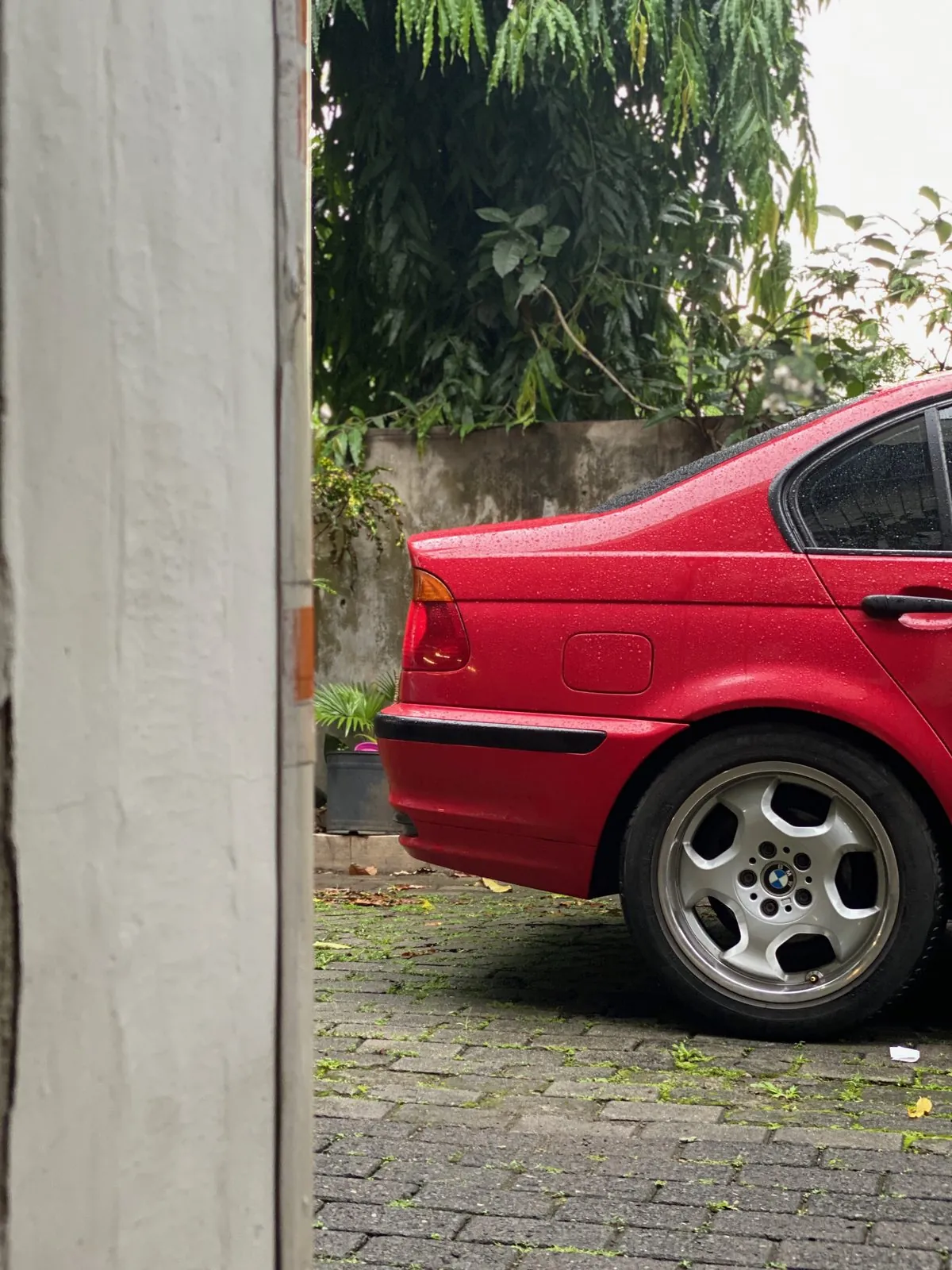 Red BMW E46 rear quarter and wheel beside the yard wall