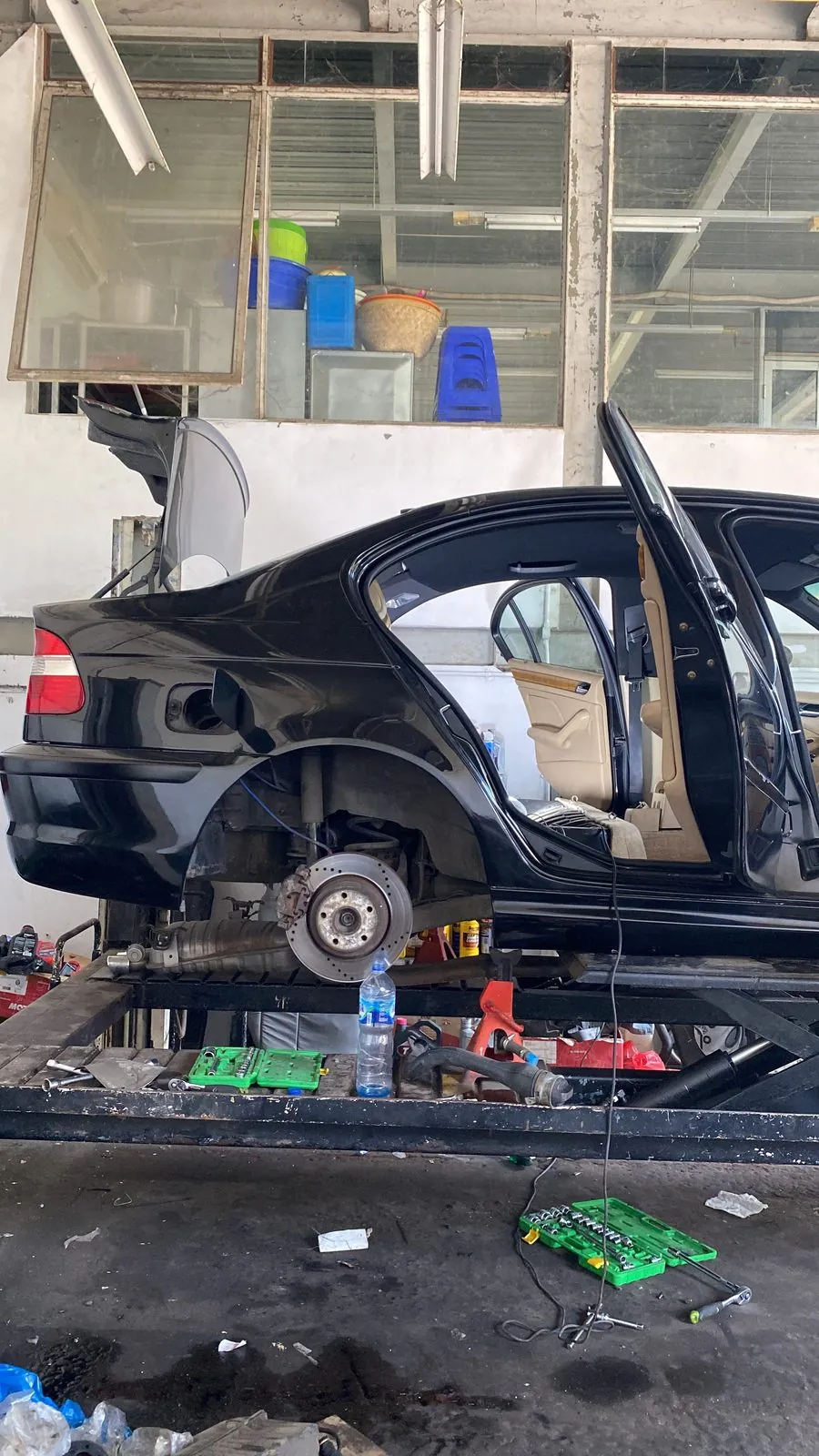 Black E46 on the lift with the rear wheel off and the interior being stripped