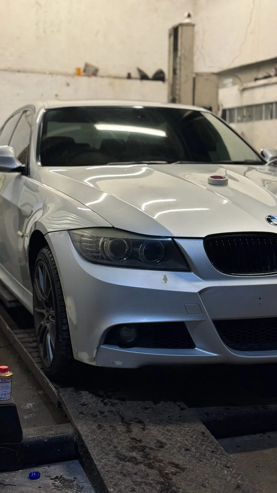 Silver BMW E90 LCI sedan on a ramp in the workshop, front view with the bonnet closed