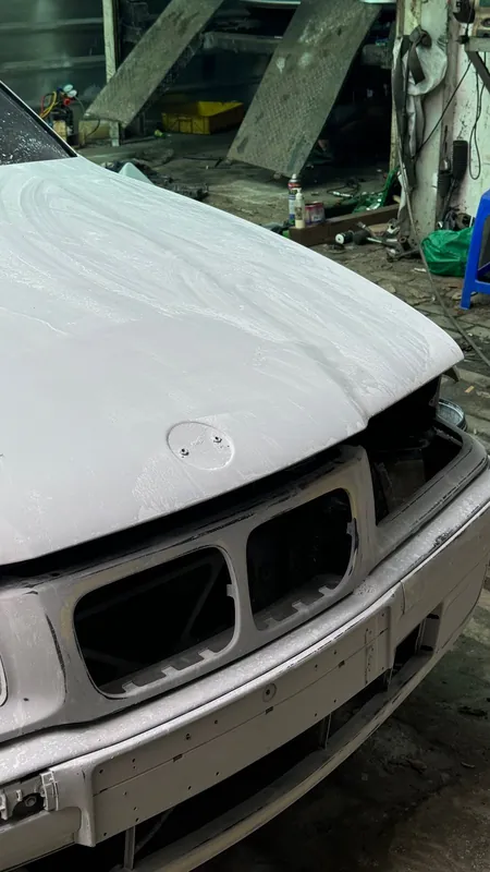 Front of the white-primed E36 with bumper and headlights removed, kidney grille openings bare
