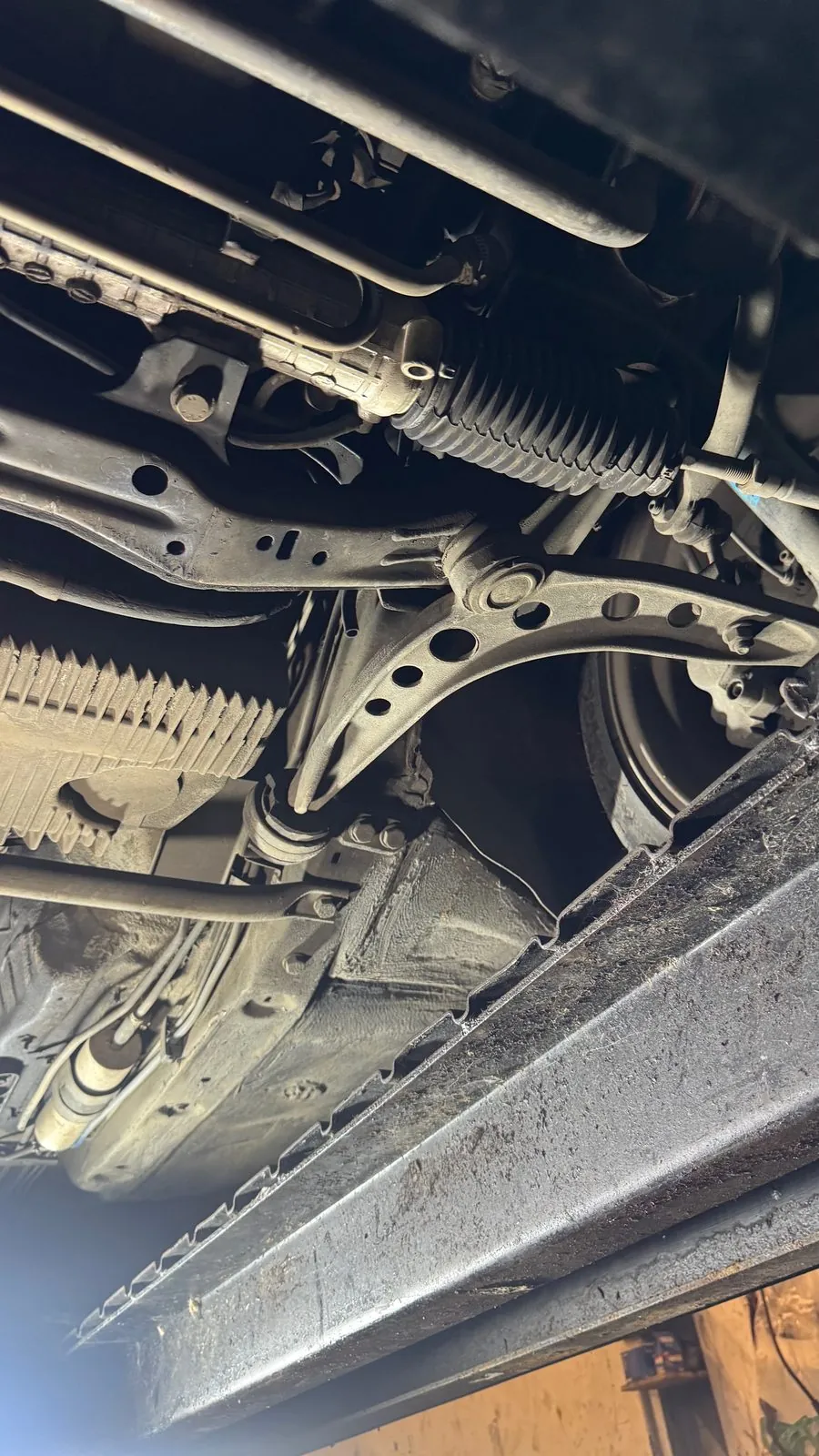 Underside of an older BMW on a lift: steering rack, front lower arm and sill