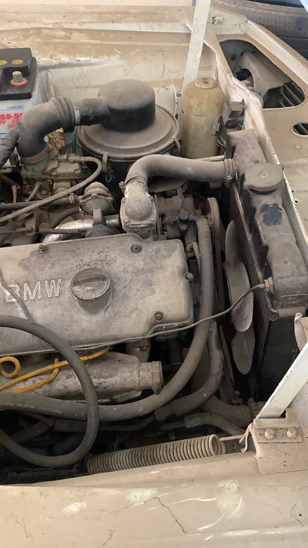 Dusty four-cylinder engine bay of an old BMW saloon with BMW cam cover lettering, carburettor