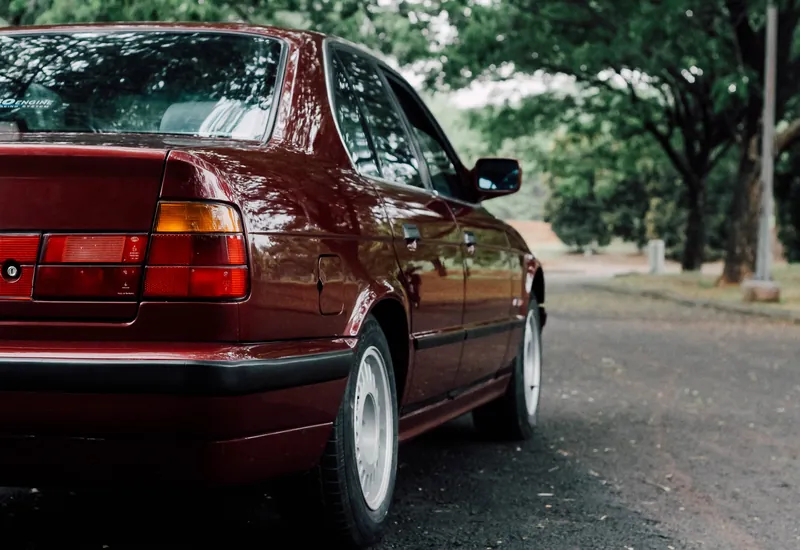 Maroon BMW E34 from the rear three-quarter on a tree-lined road
