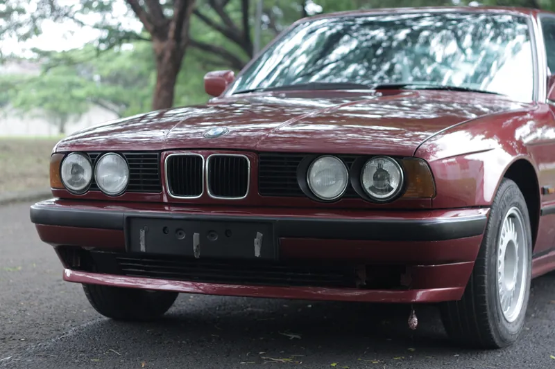 Front of a maroon BMW E34 on a tree-lined road