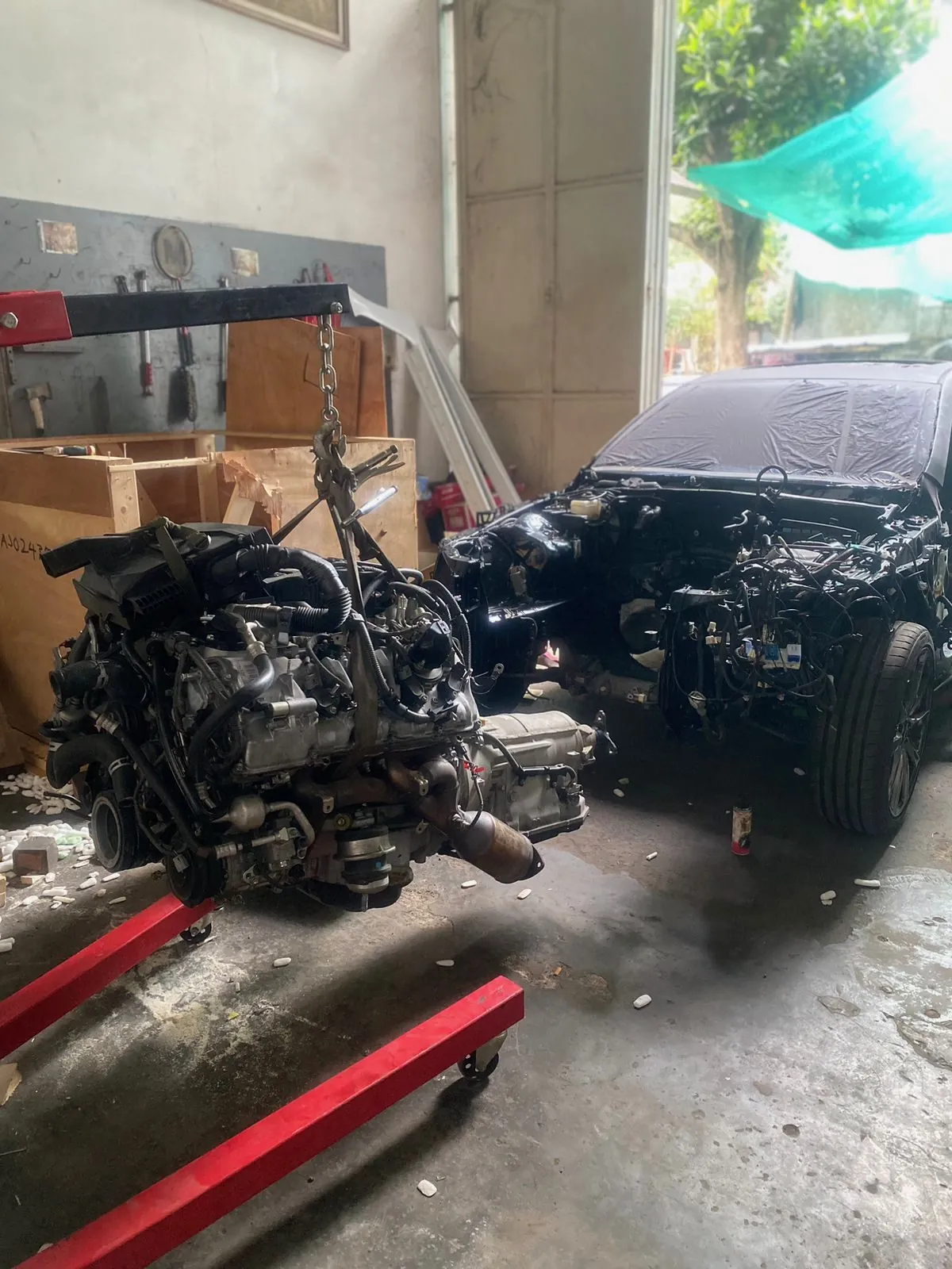Engine and gearbox hanging from an engine crane beside the car in the workshop