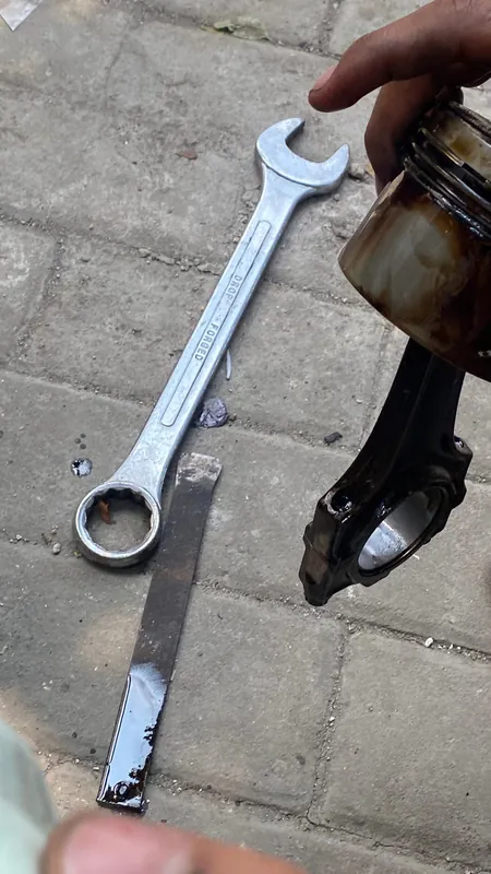 Connecting rod and piston beside a spanner on the paving
