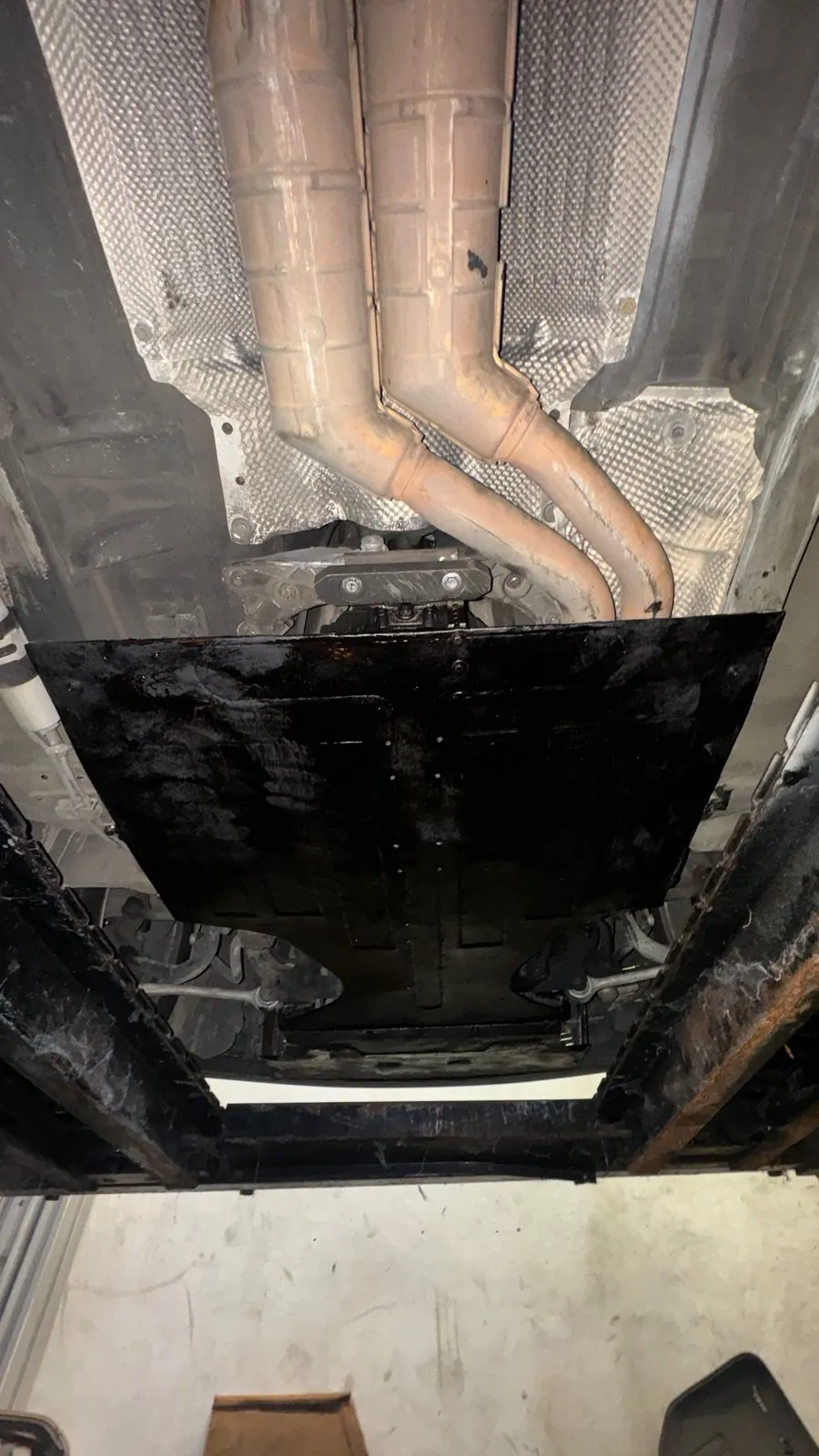 Underside of a car on a lift: twin exhaust headers and a black underbody plate