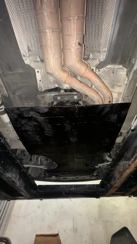 Underside of a car on a lift: twin exhaust headers and a black underbody plate