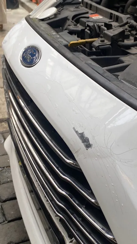 White Ford front grille and emblem with a scratched, cracked bumper edge