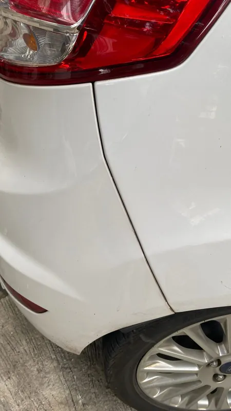 Rear quarter, tail lamp and wheel of a white Ford hatchback with a crease in the wing
