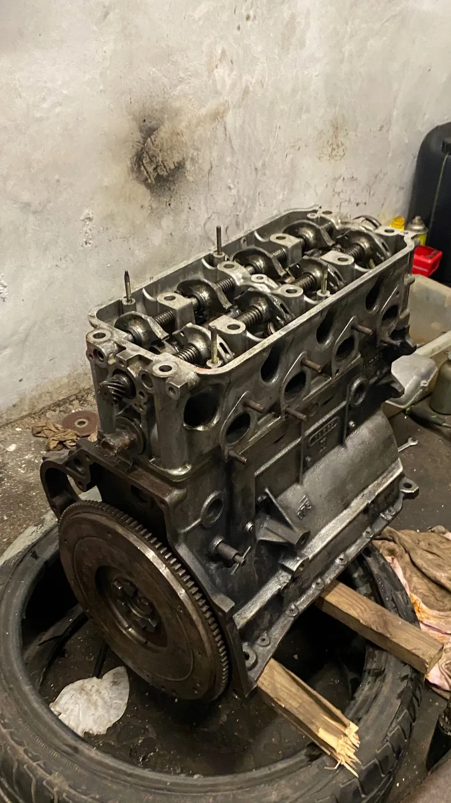 Four-cylinder engine with the head fitted and the flywheel on, resting on a tyre