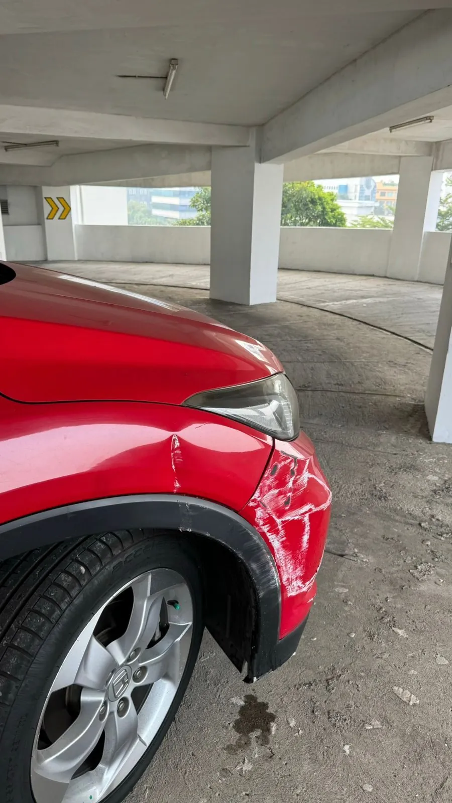 Front wing of red Honda HR-V with a dent and scuffed paint above the wheel, under a car park roof