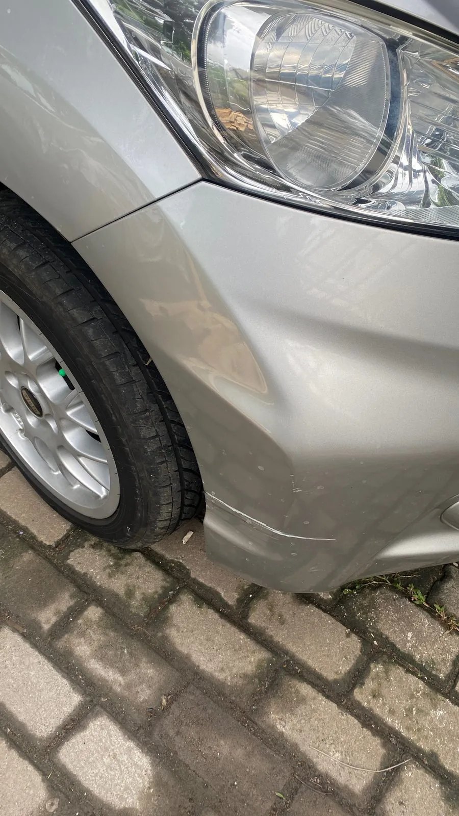 Dented, creased front wing and bumper corner of a silver Honda MPV