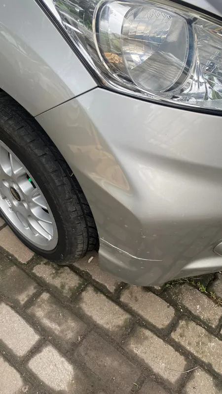 Dented, creased front wing and bumper corner of a silver Honda MPV