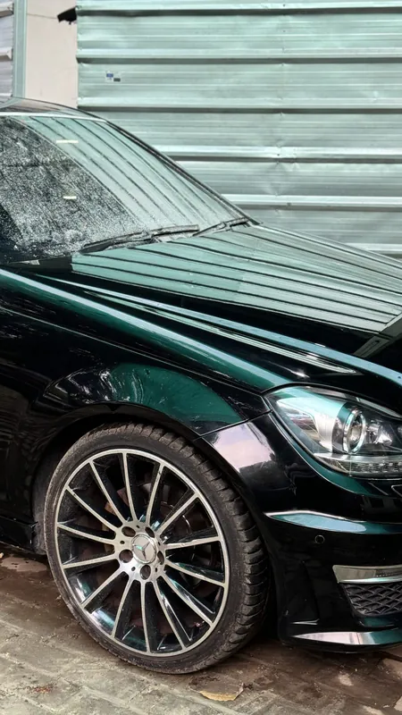 Front wing and multi-spoke alloy wheel of black Mercedes C200, wet bonnet