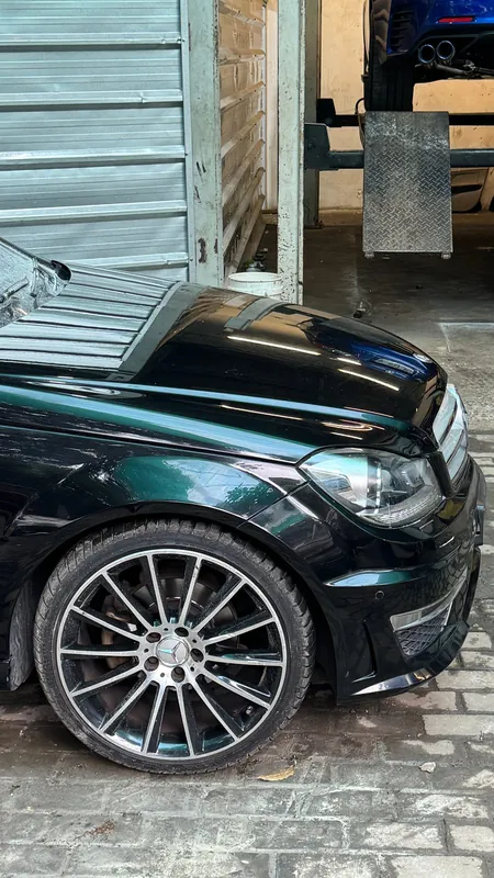 Front wing and multi-spoke alloy of black Mercedes C200 in the workshop doorway