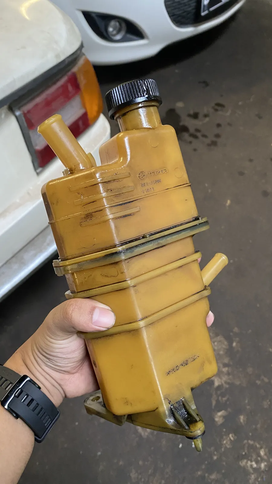 Hand holding a removed power steering fluid reservoir