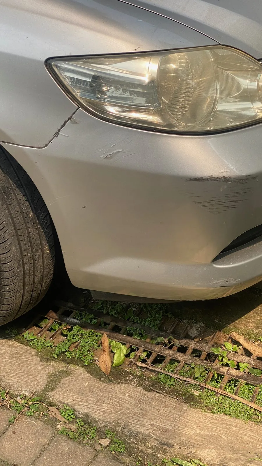 Scraped front bumper and wing edge below the headlight of a silver sedan