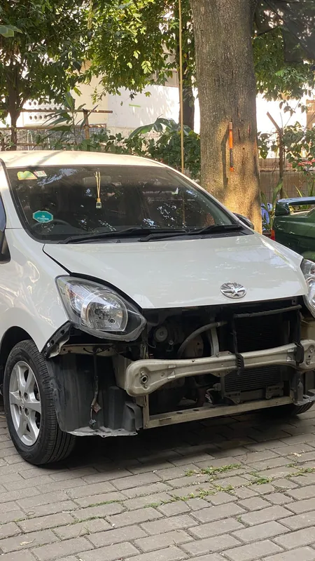 White Toyota Agya with the front bumper and headlight removed, radiator support exposed