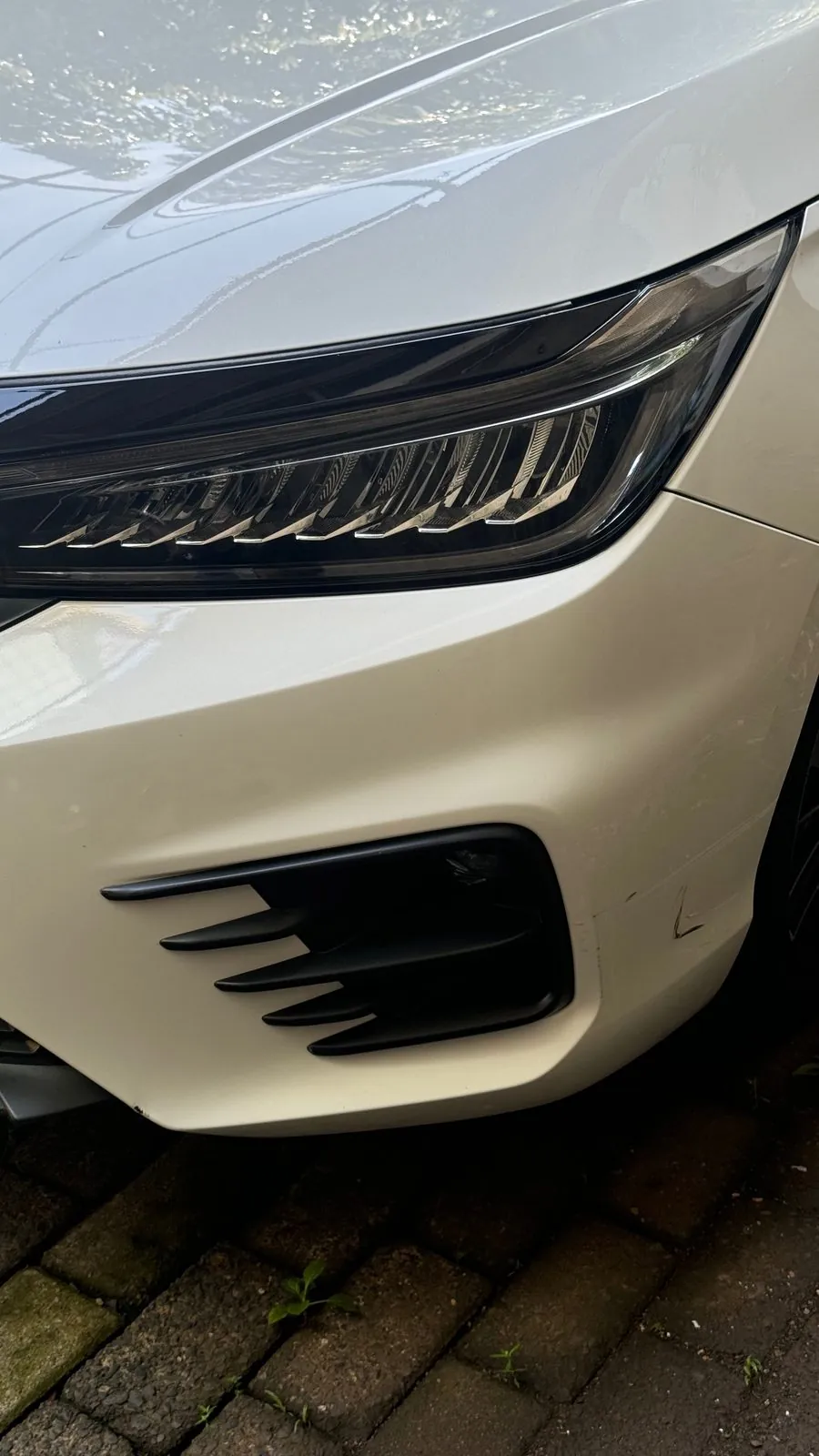 Front bumper corner and headlight of a white sedan with a scratch