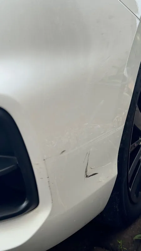 Scratched front bumper corner and wheel arch of the white sedan