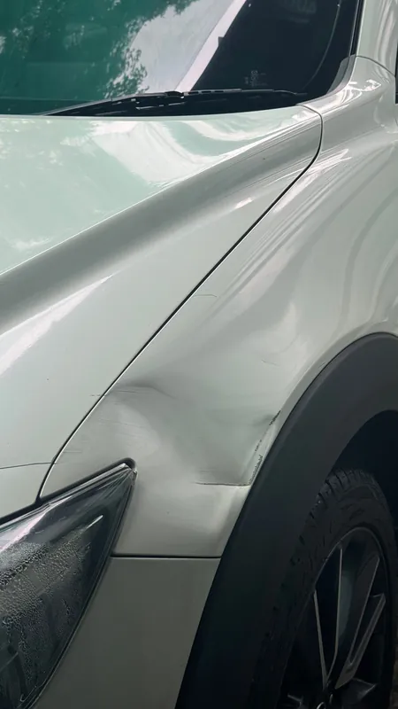 Dent in the front wing of a white SUV above the headlight